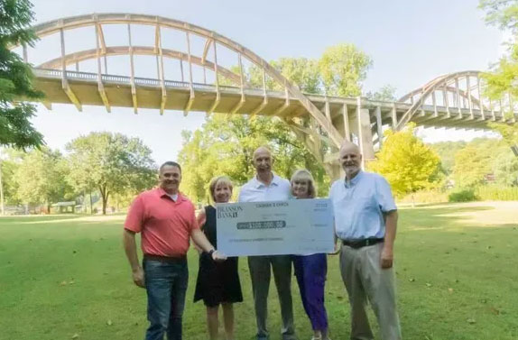 Group of donors standing in front of cotter bridge holding a large check