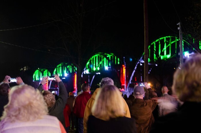 people watch the Peitz River Lights on the Cotter Bridge in festive Christmas colors of red, green, and white