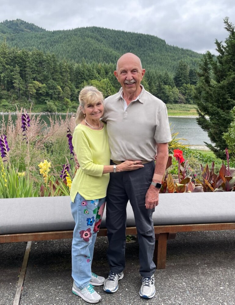 Jan and Peter Peitz standing side by side with a beautiful backdrop of mountains and flowers